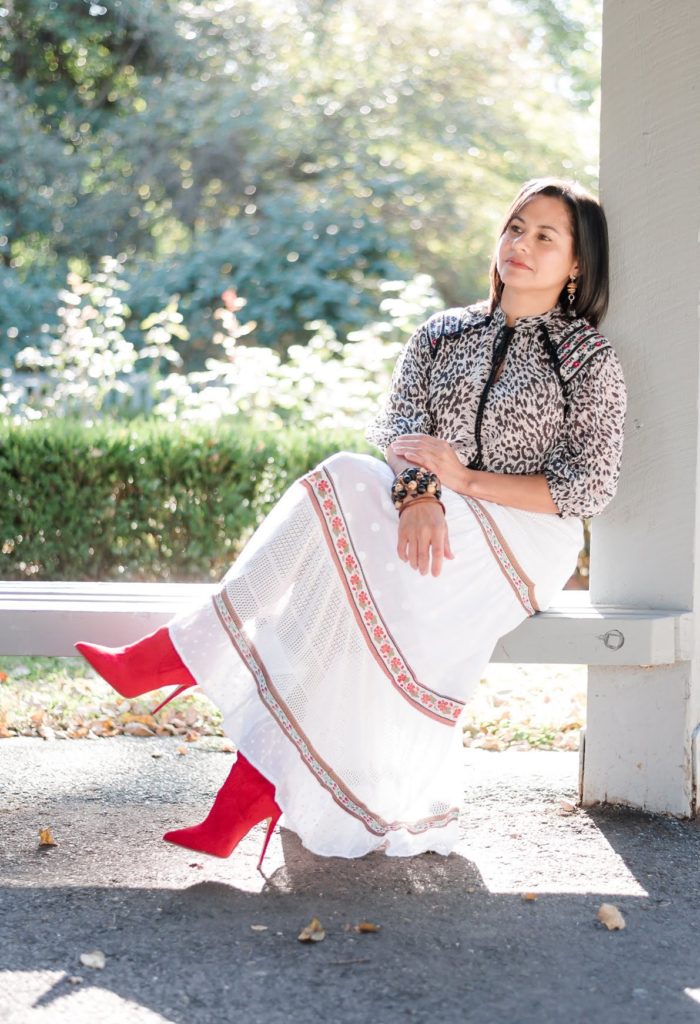 a mom sitting under the sun relaxing dressed in white maxi skirt, animal print top, over the knee red boots, vidart & life wood bracelets