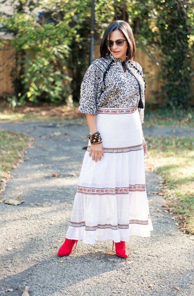 a girl standing up and looking down to the ground dressed in a animal print top, white maxi skirt wearing red boots and vidart & life bracelets