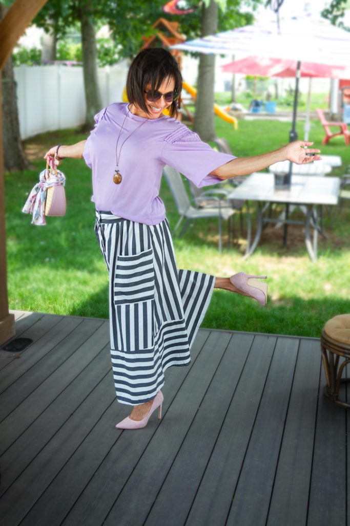 Vida DeCaro is playful challenging herself standing in one foot wearing pink high heels, stripe skirt and Vidart and Life long necklace. 