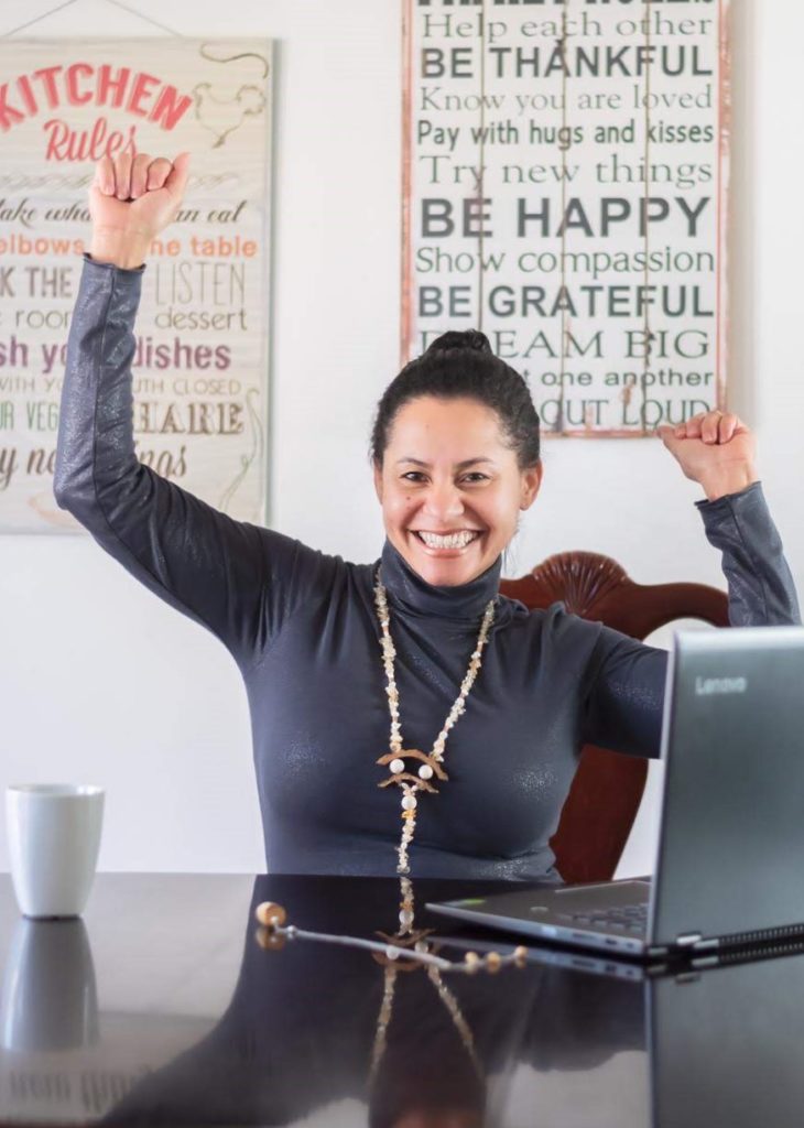 Vida sitting on her kitchen table wearing a long wood necklace celebrating for  finish writing a first blog post 