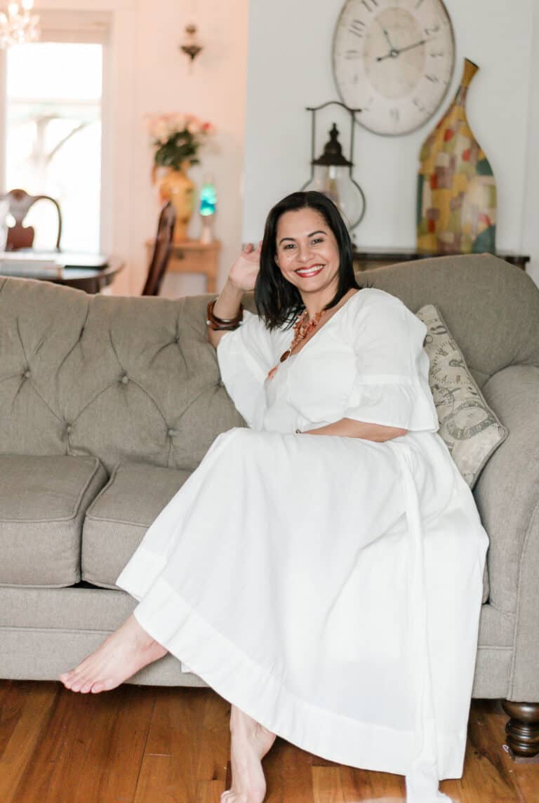 Vida DeOlivier: A stay-at-home mom entrepreneur sitting on the sofa of her living room, smilingly.