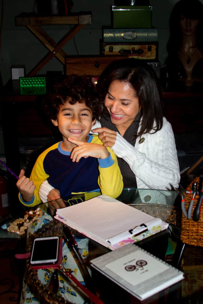 An entrepreneur mom sitting at the table with her son having a happy time drawing jewelry.