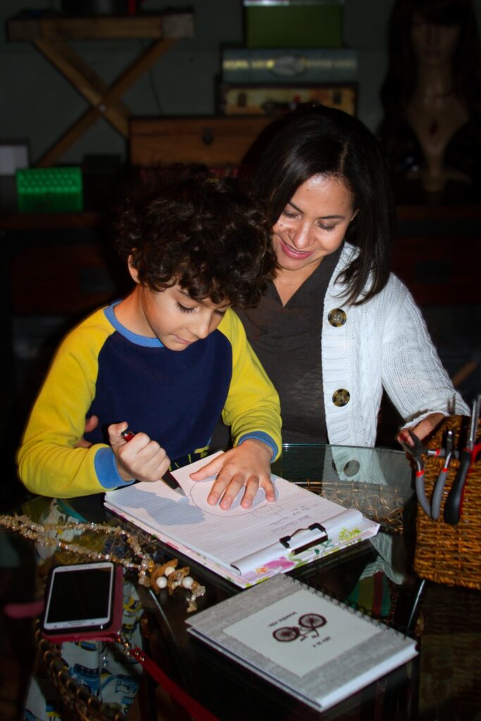 High-Performance Stay at Home Entrepreneur Vida DeOlivier sitting at a table on her workplace drawing with her old son.